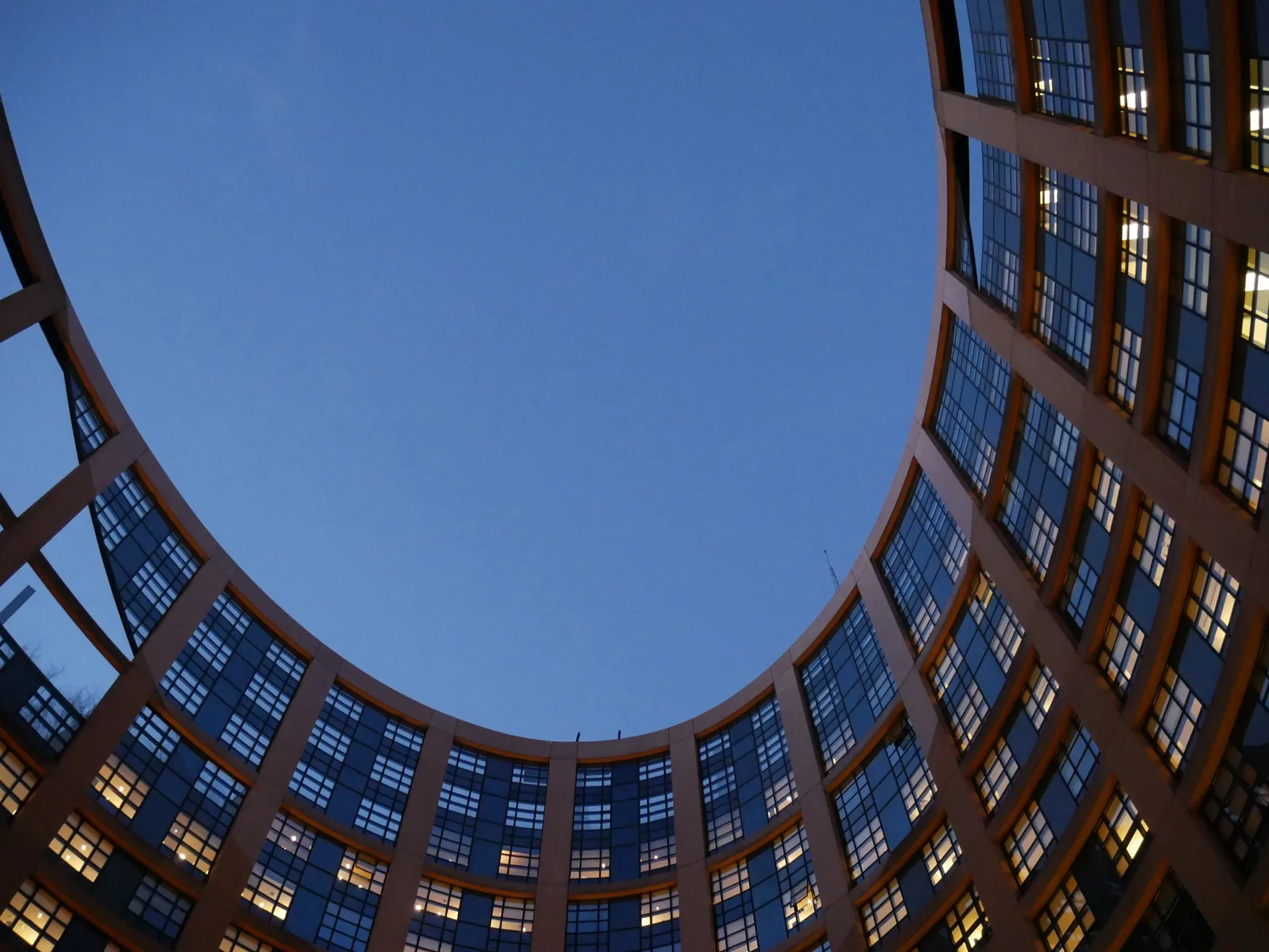 Bâtiment moderne arrondi vu en contre-plongée sous un ciel bleu crépusculaire