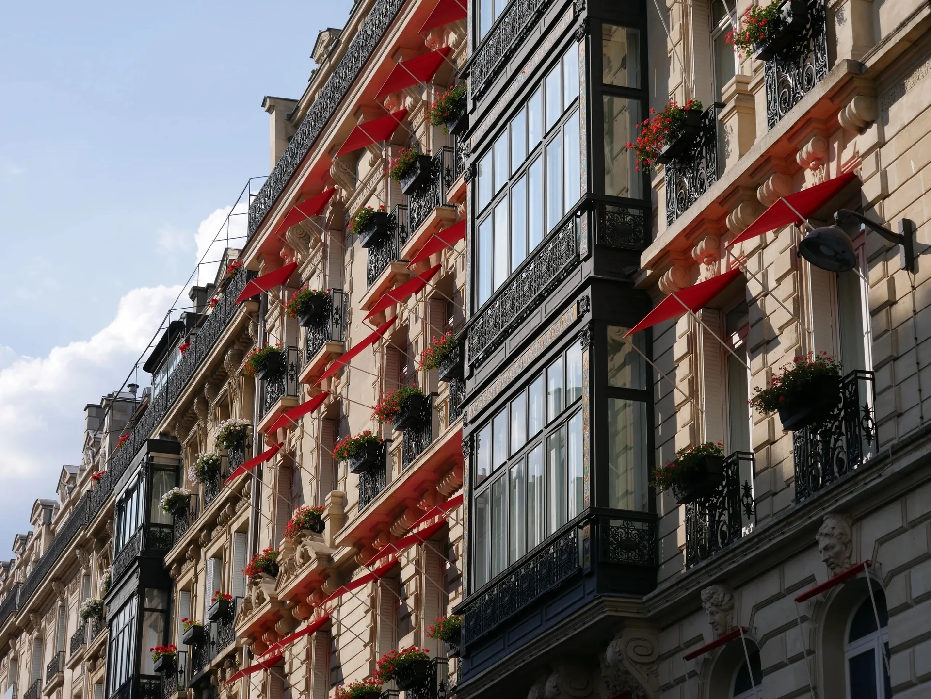 Façade haussmannienne parisienne avec balcons en fer forgé et stores rouges