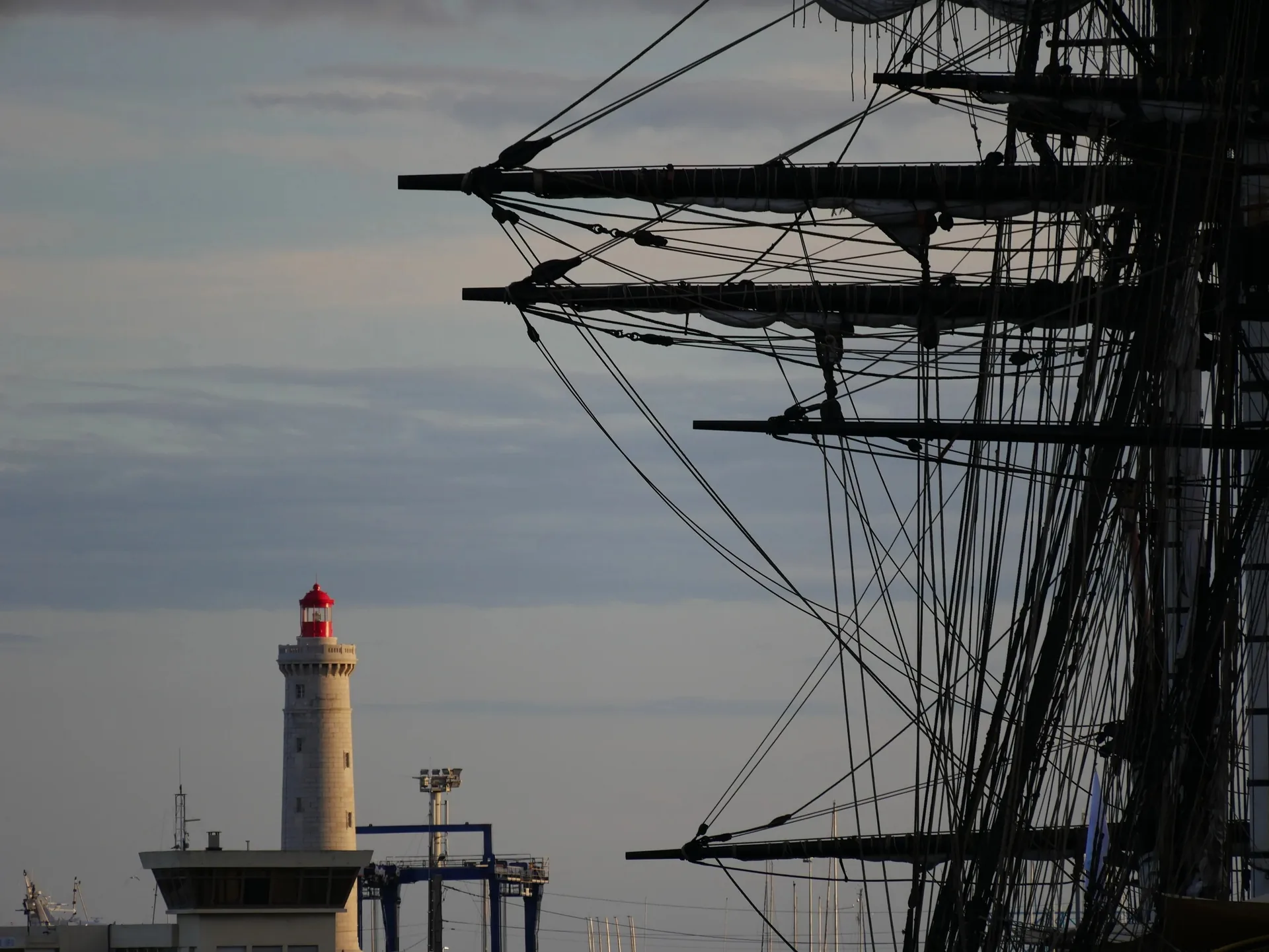Mâts d'un grand voilier et phare de Sète au crépuscule