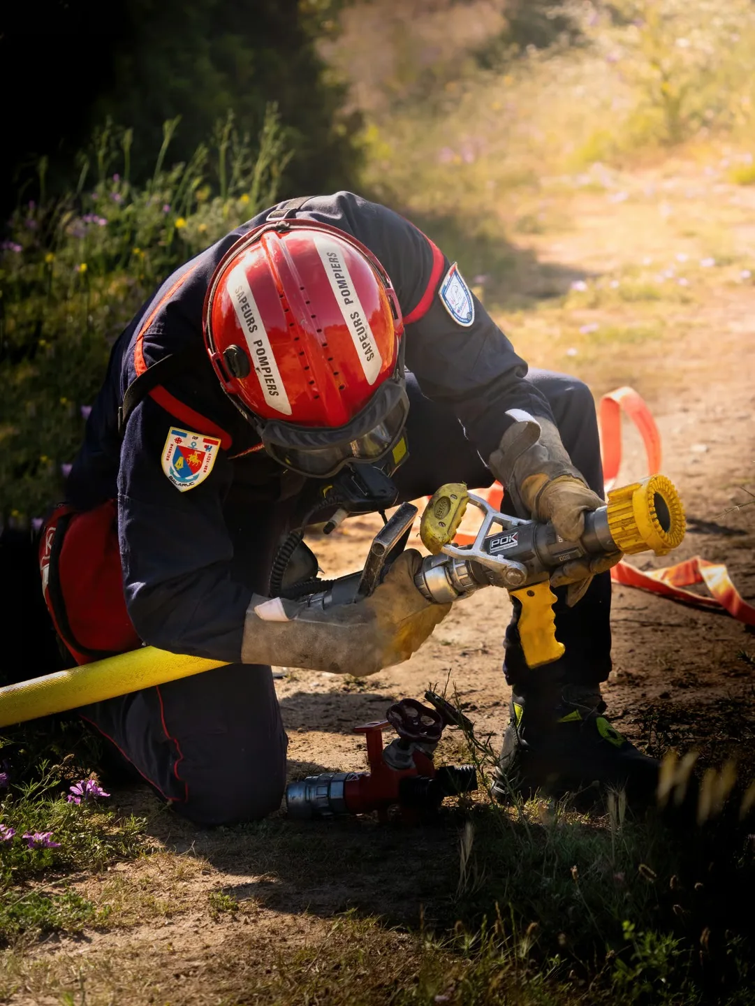 Pompier au sol maniant une lance à incendie