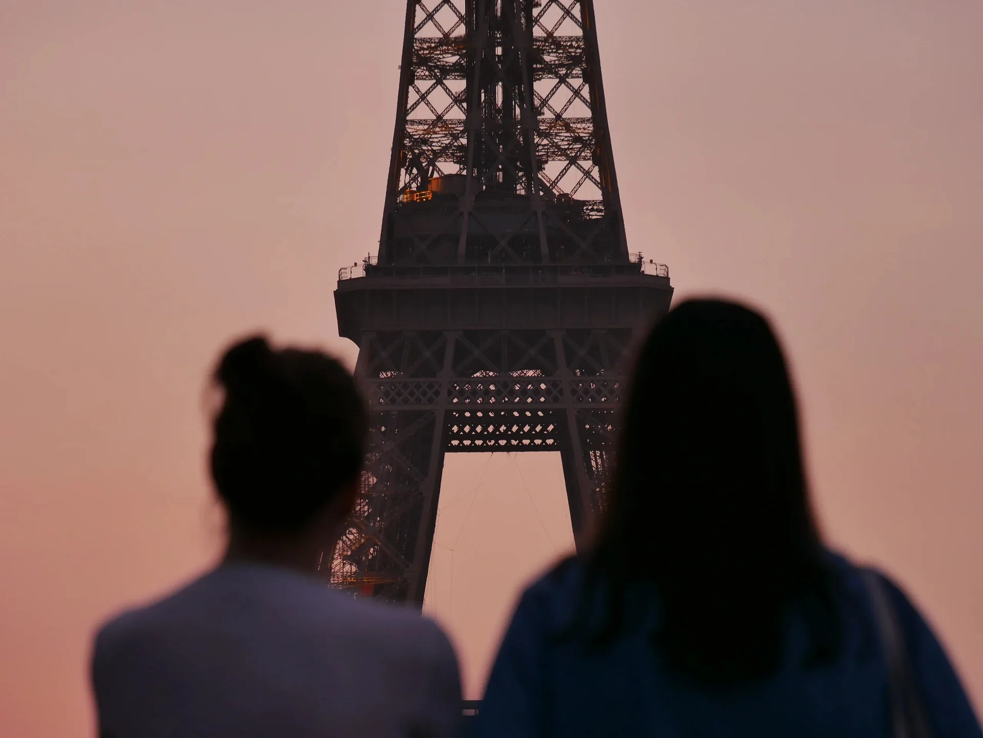 Couple en silhouette contemplant la Tour Eiffel dans un ciel rose au coucher du soleil