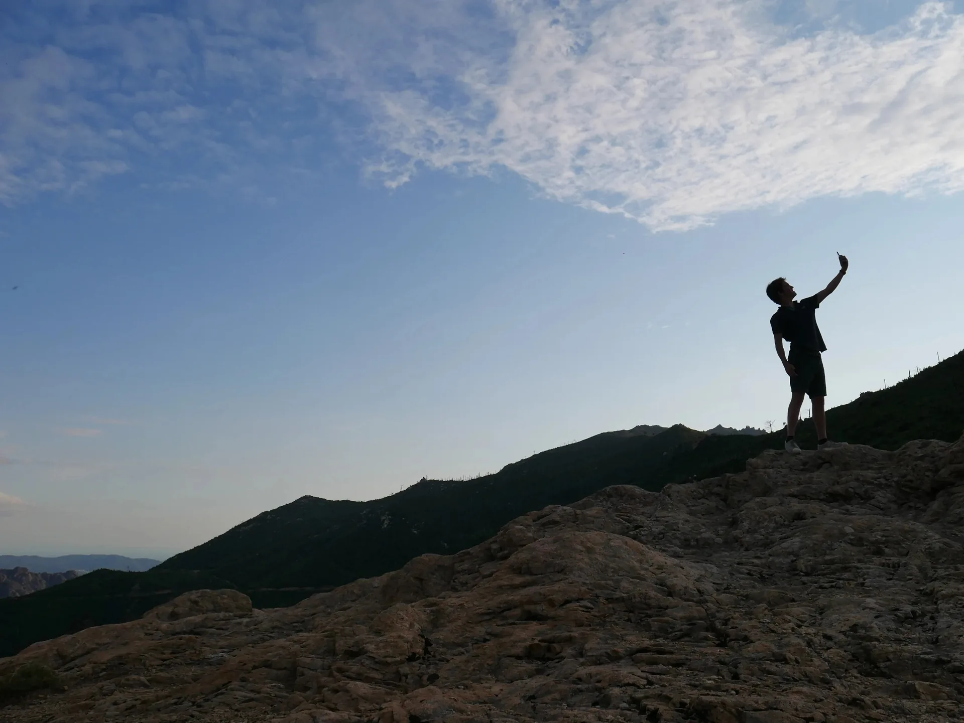 Silhouette d'un randonneur prenant un selfie au sommet d'un rocher en Corse